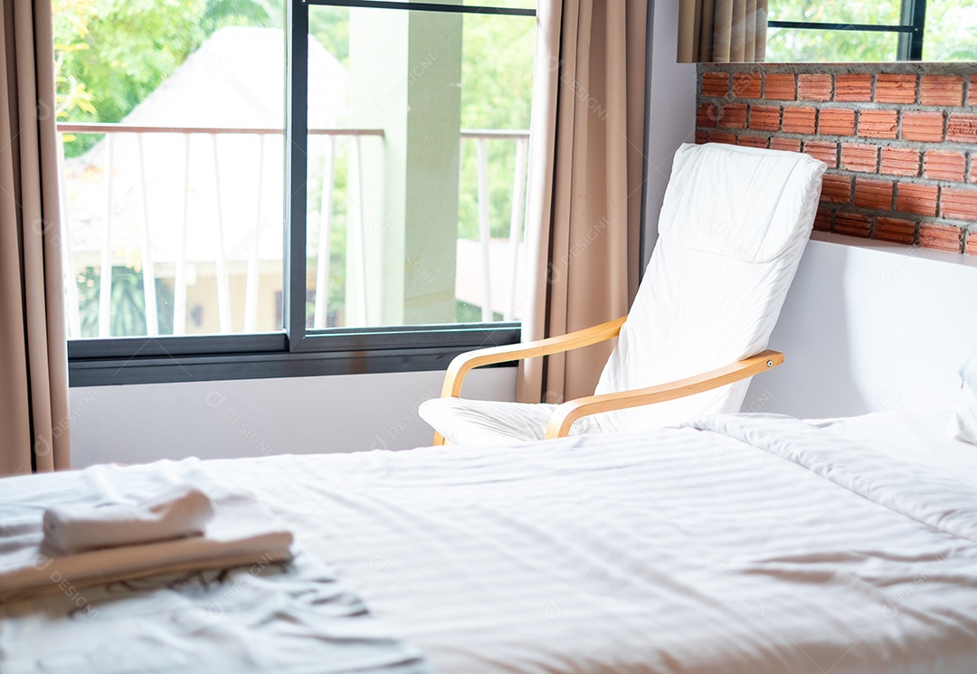Cadeira de madeira branca e cama branca perto das janelas em uma sala de estilo loft em um resort, tempo de relaxamento, férias