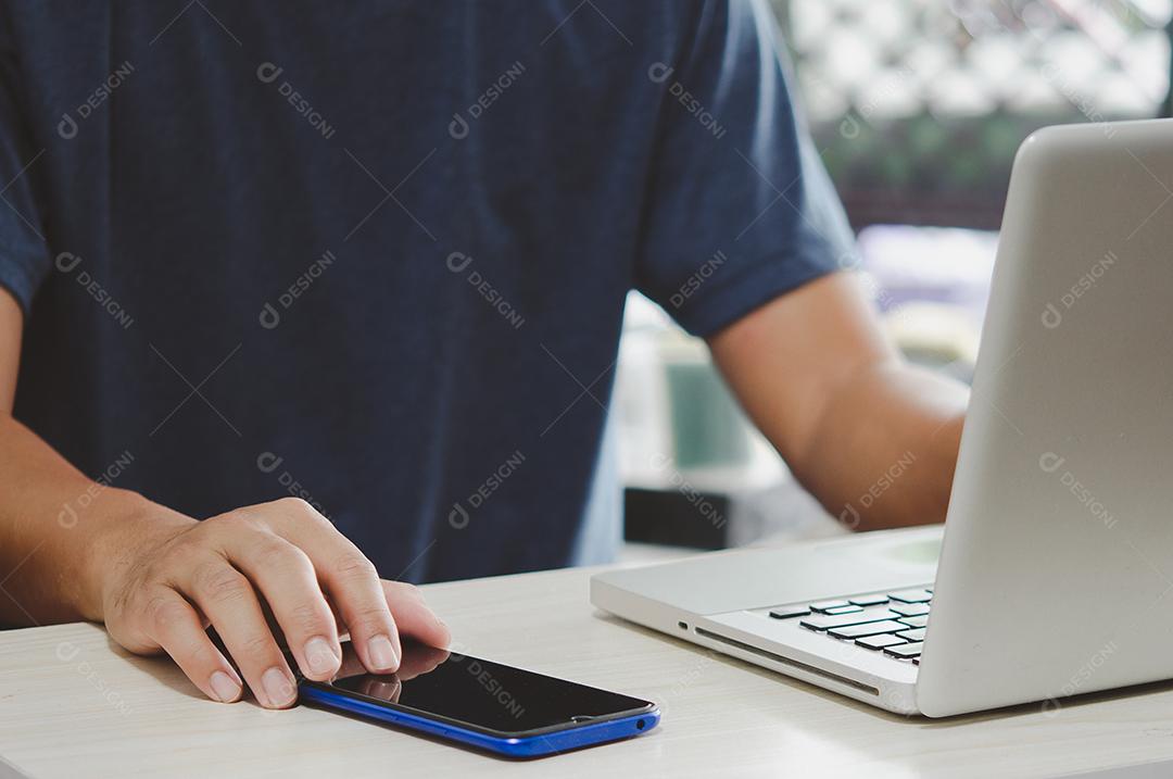 Homem trabalhando na mesa do computador pressionando o celular