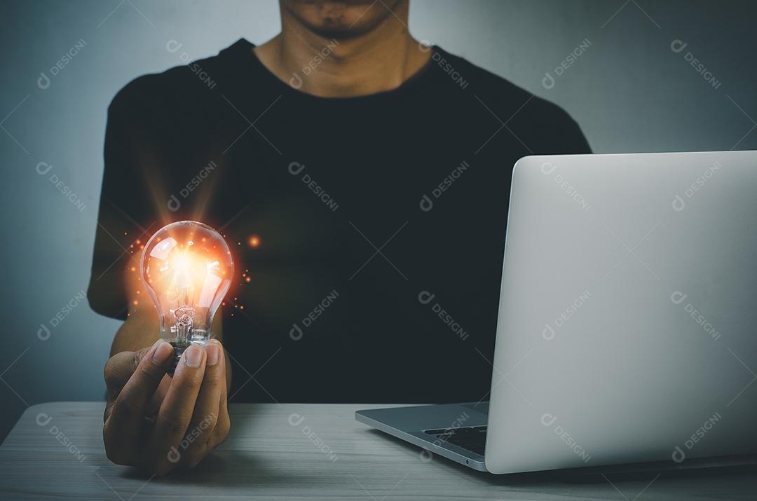 Mão segurando ideias de lâmpada grande inspiração e inovação na mesa com o computador portátil.