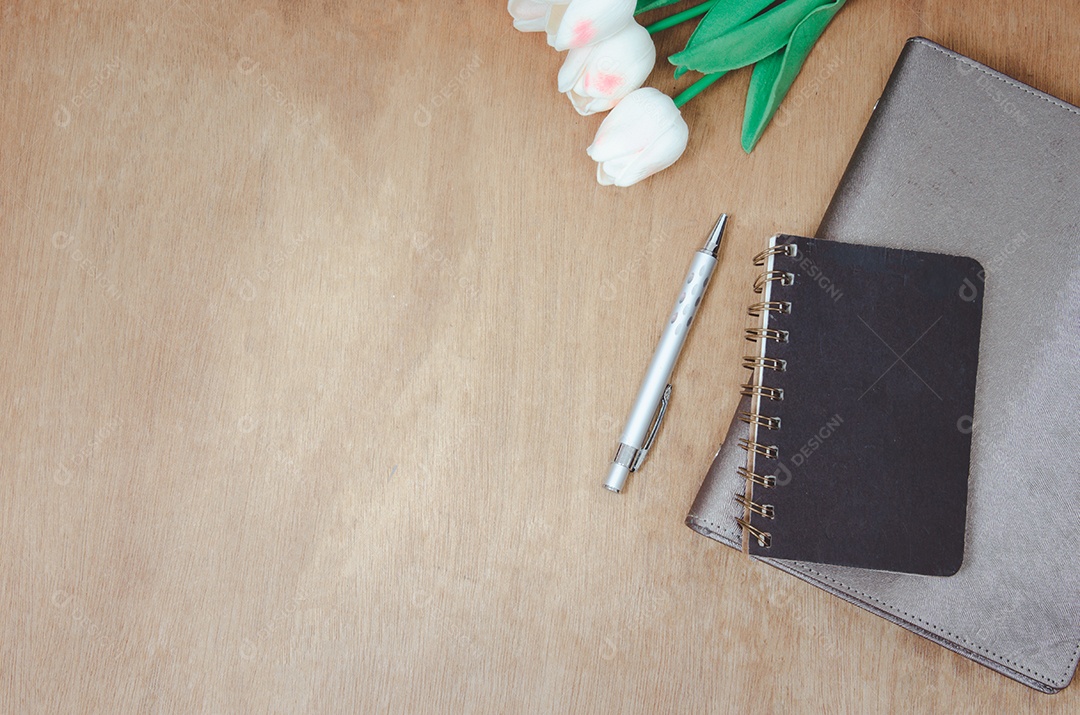 Caderno plano de vista superior e flor e caneta na mesa de madeira.