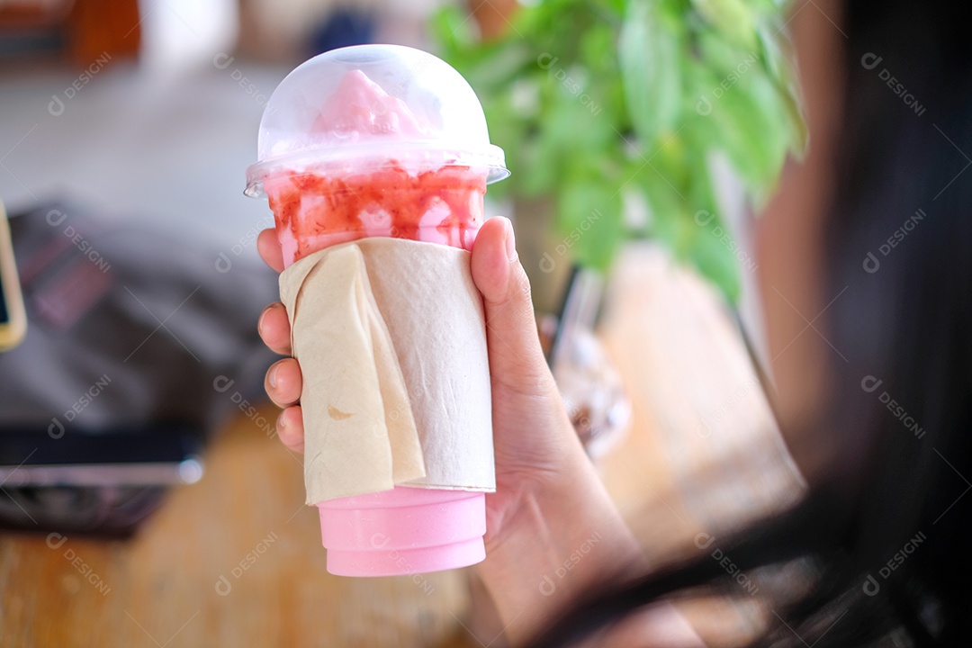 Mão segurando uma caneca de milk-shake de smoothie de morango embrulhada em papel de seda vazio, cafeteria