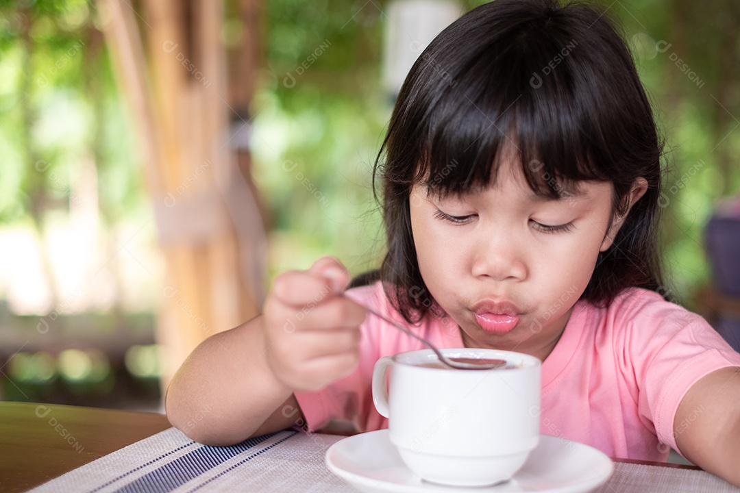 Linda garota asiática vestindo uma camisa rosa. Ele estava soprando Ovantine quente de sua colher durante o café da manhã.