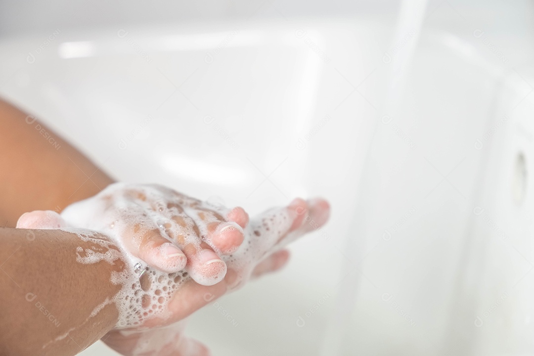 Criança lavando as mãos com sabão branco em uma pia branca no banheiro.