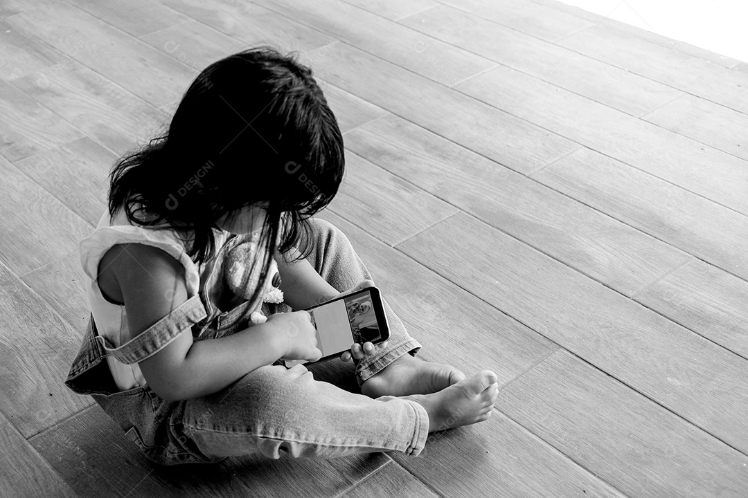 Menina asiática bonitinha jogando telefone inteligente, criança viciada em celular imagem preto e branco