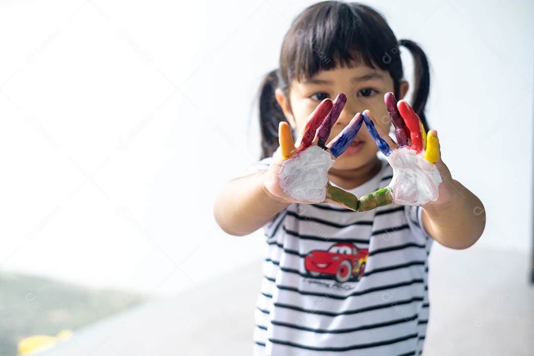 Menina asiática pintando seus próprios dedos para fazer arte, multicolorida, lição de casa, engraçada