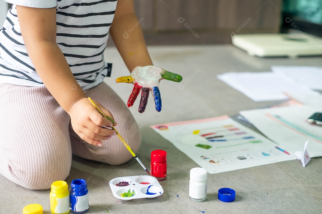 Menina asiática pintando seus próprios dedos para fazer arte, multicolorida, lição de casa, engraçada