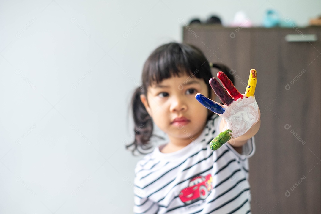 Menina asiática pintando seus próprios dedos para fazer arte, multicolorida, lição de casa, engraçada