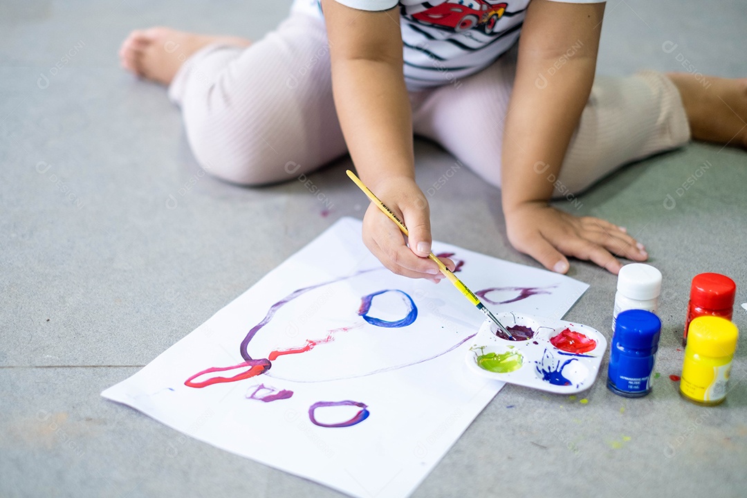 Menina asiática pintando seus próprios dedos para fazer arte, multicolorida, lição de casa, engraçada
