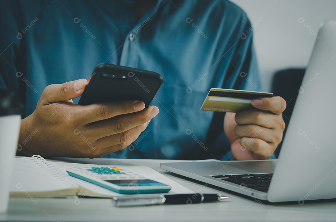 Mão de homem segurando cartão de crédito e telefone celular compras on-line e-commerce e internet banking na mesa.