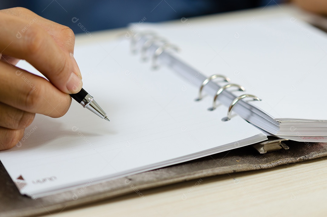 Feche segurando uma caneta e escrevendo no caderno.