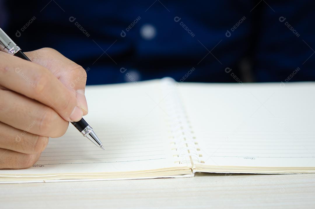 Feche segurando uma caneta e escrevendo no caderno.