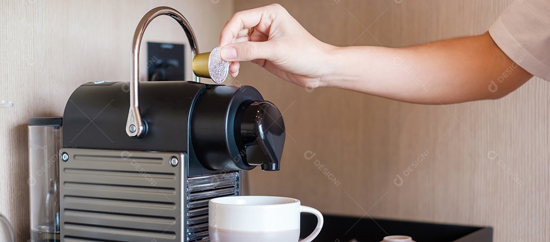 Mão fazendo café expresso por máquina de café com cápsulas na mesa de madeira