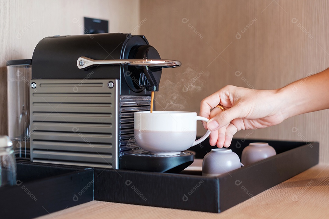 Mão fazendo café expresso por máquina de café com cápsulas na mesa de madeira