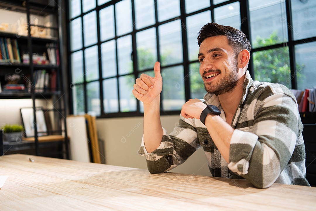 Jovem designer criativo mostrando o polegar para cima e sorrindo na mesa