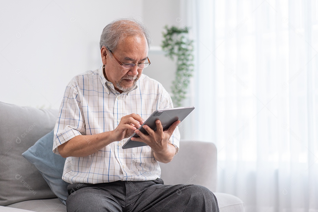 Avô asiático usando tablet digital sentado no sofá