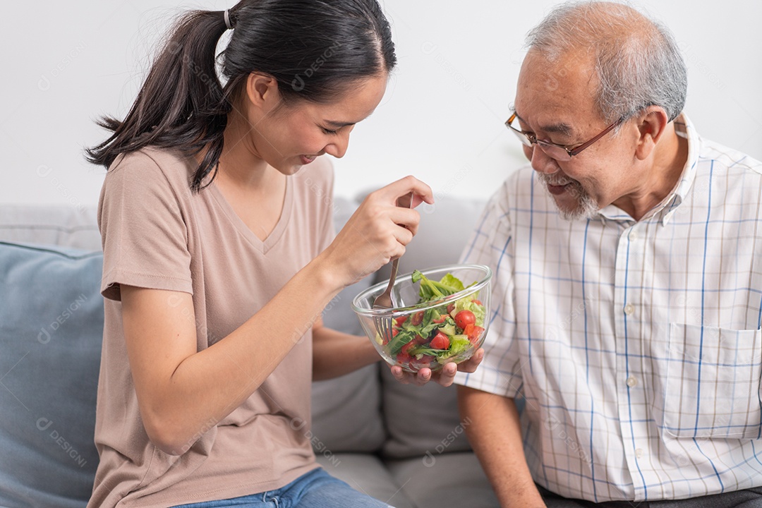 Filha jovem asiática servindo e alimentando comida para pai sênior