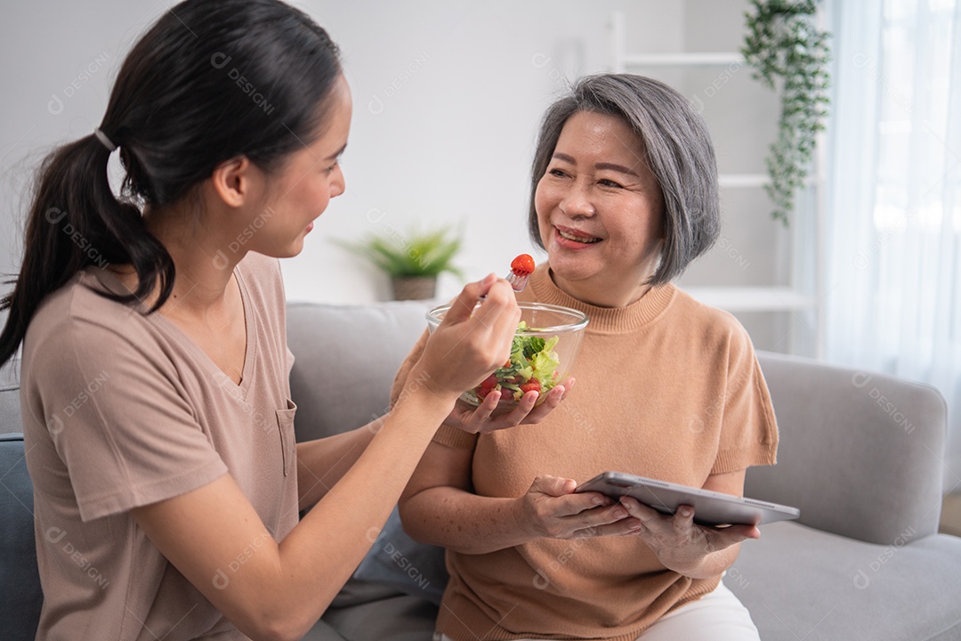 Filha asiática jovem servindo e alimentando comida para mãe sênior