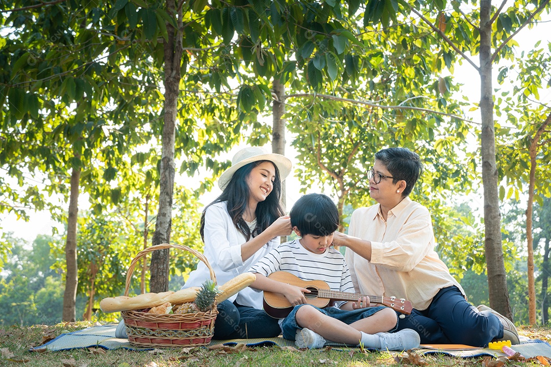 Feliz mãe asiática e avó assistindo filho tocando ukulele