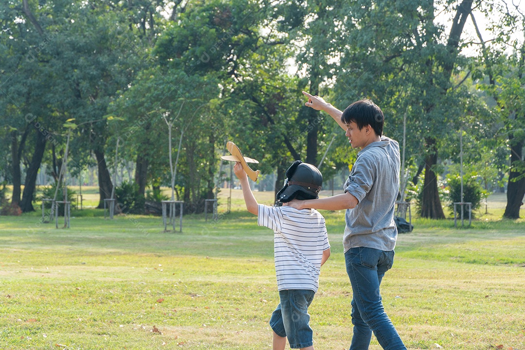 Feliz pai asiático jogando avião de papel com filho no parque