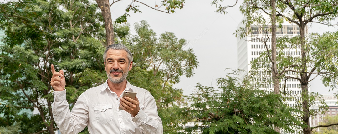 Homem sênior caucasiano usando telefone celular enquanto relaxa no parque.