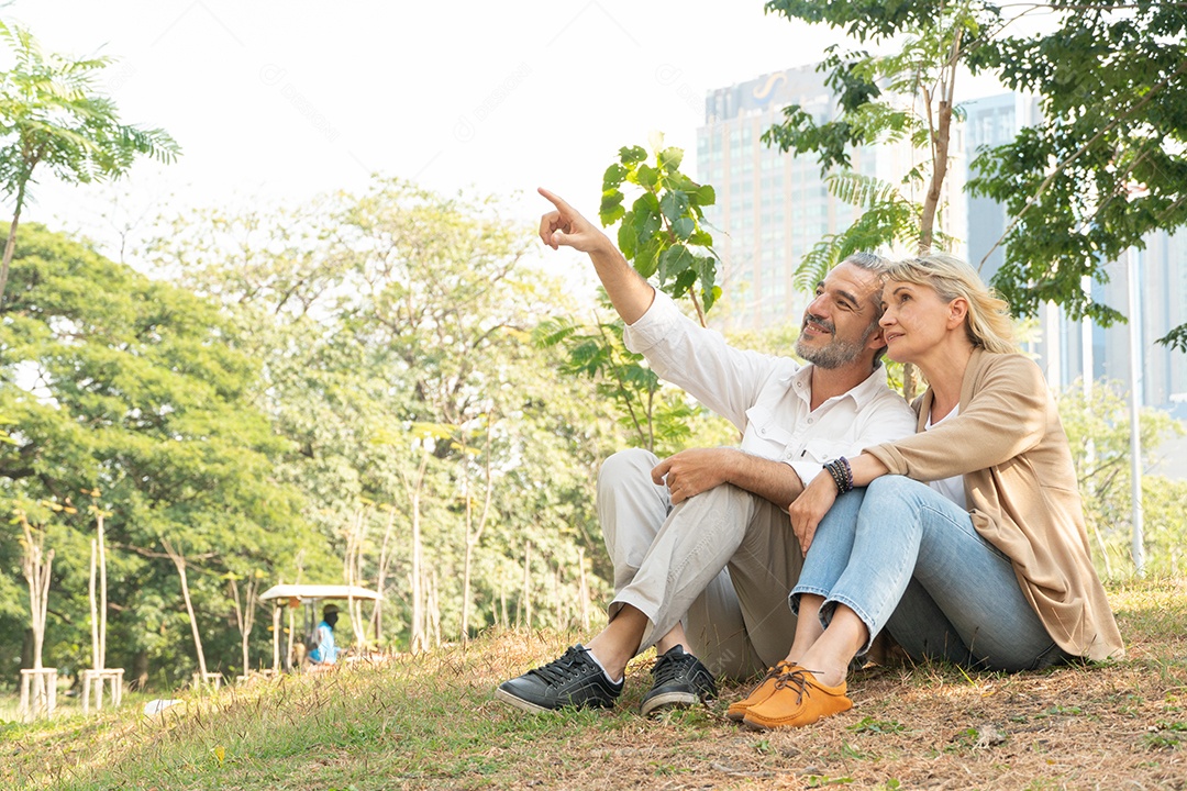 Casal sênior relaxa sentado e conversando na grama do parque