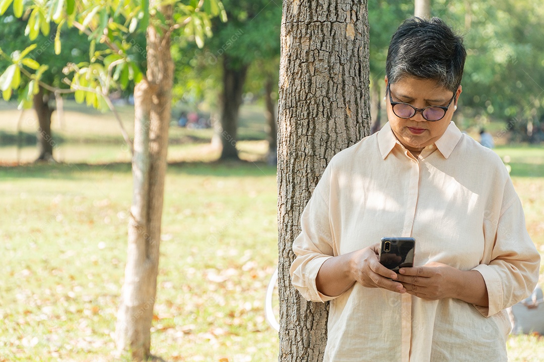 Mulher sênior asiática em pé na árvore no parque