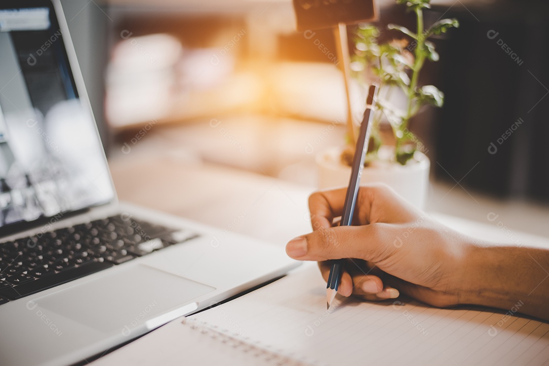 As pessoas usam lápis para desenhar e anotar no bloco de notas. Computador portátil e pequenos elementos de vasos de plantas. Conceito de negócios e tecnologia.