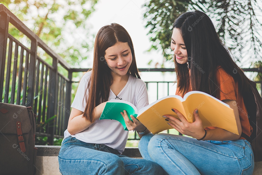 Duas garotas de beleza asiática lendo e ensinando livros para o exame final juntos. Estudante sorrindo e sentado na escada. Educação e volta ao conceito de escola. Estilos de vida e tema de retrato de pessoas.