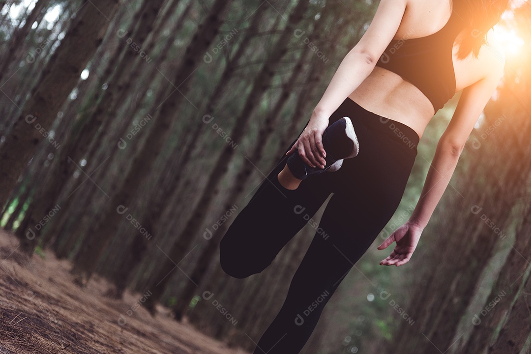 Feche a parte inferior do corpo da mulher fazendo ioga e esticando as pernas antes de correr na floresta ao ar livre. Conceito de esportes e natureza. Estilo de vida e conceito de atividade.