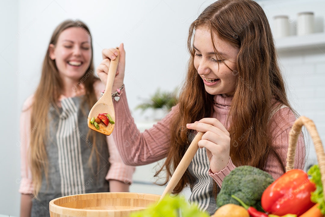 Mãe assistindo filha cozinhar salada caseira