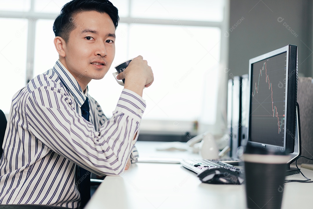 Comerciante da bolsa asiática bebendo café e observando o gráfico no monitor