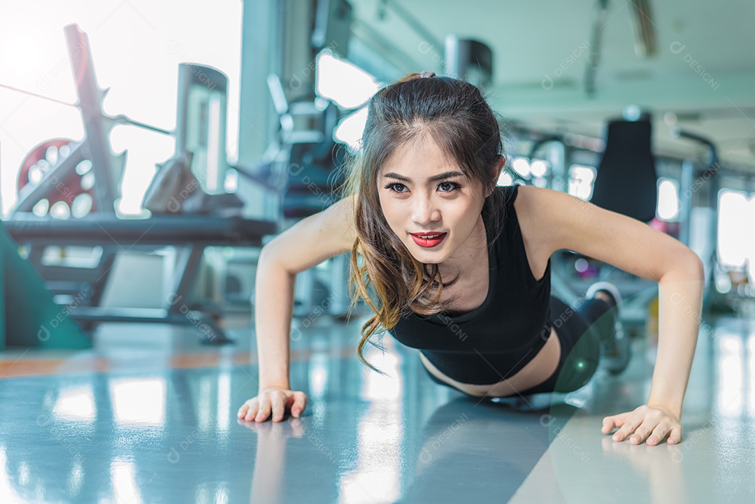 A menina asiática da aptidão da mulher faz push ups no ginásio da aptidão. Cuidados de saúde e conceito saudável. Tema de construção de treinamento e corpo. Conceito de força e beleza