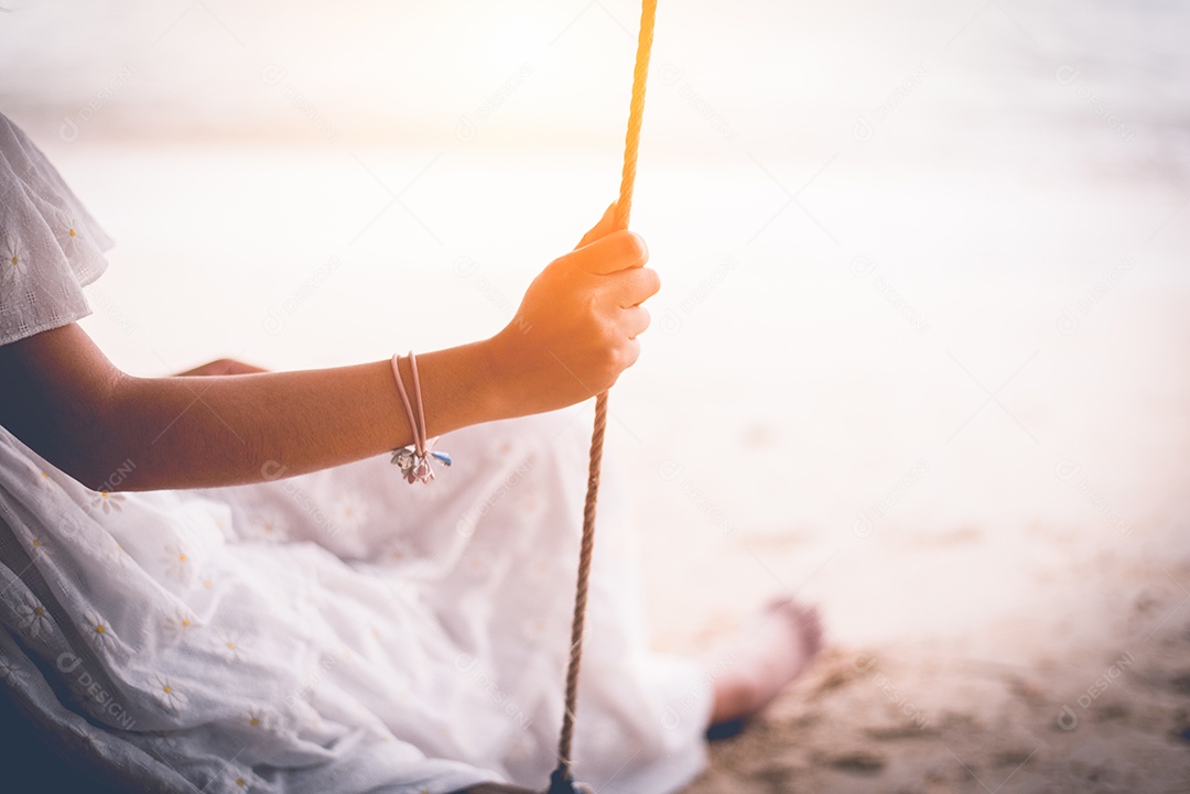 Mão de mulher asiática em vestido branco sentado no balanço na praia. Conceito de pessoas e natureza. Amor triste e conceito de falta de alguém. Tema solitário e de coração partido.