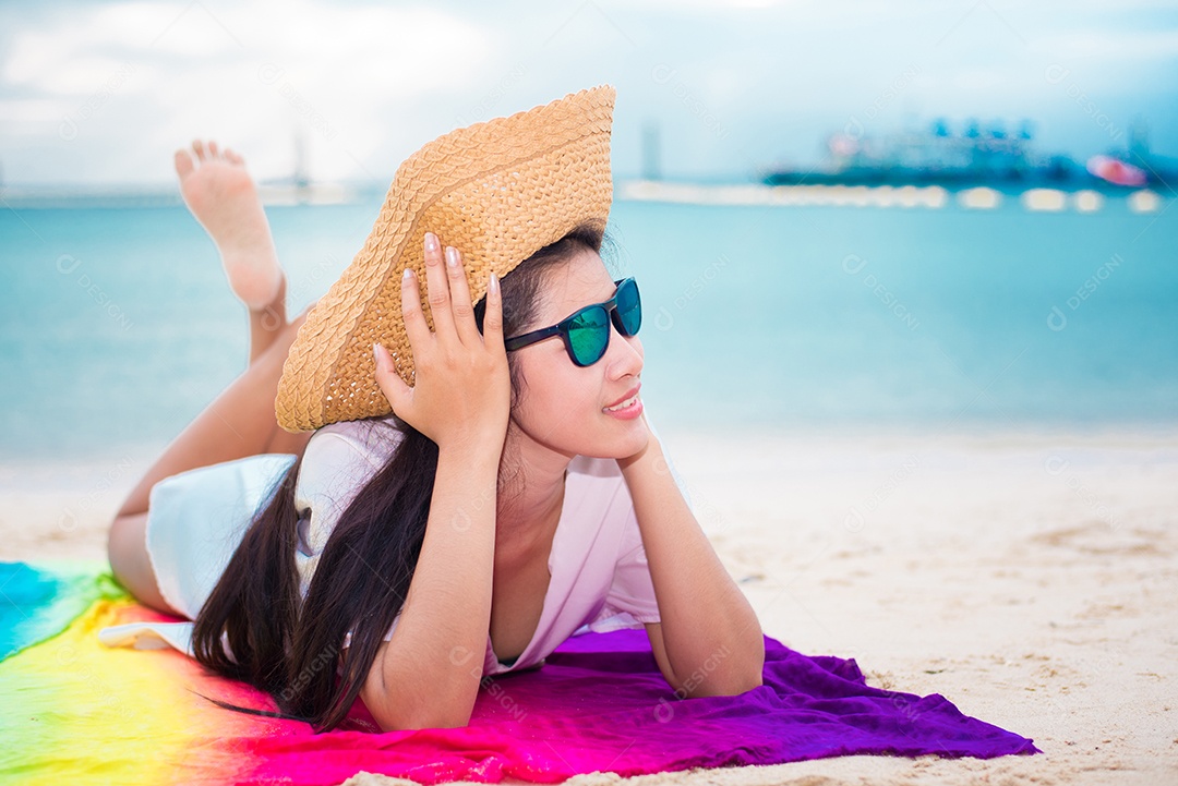 Mulher asiática em casual e chapéu de palha deitado na praia tropical com fundo do mar. Relaxe e o conceito de estilo de vida. Conceito de férias e férias. Mulher solteira e tema de felicidade.