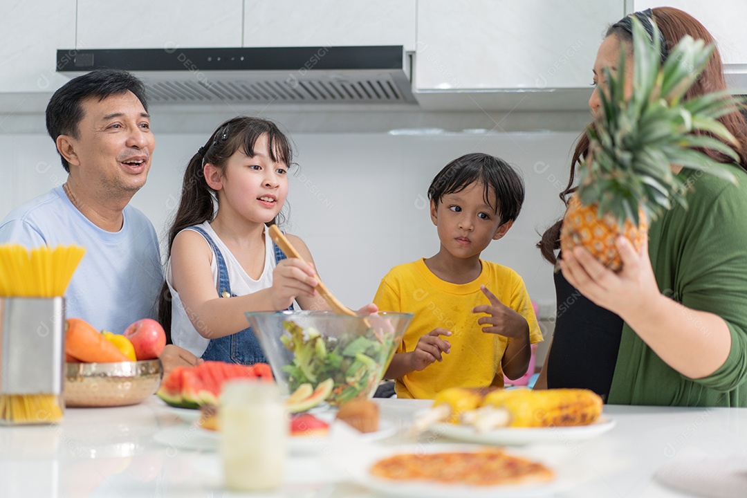Família asiática feliz fazendo salada na cozinha juntos.