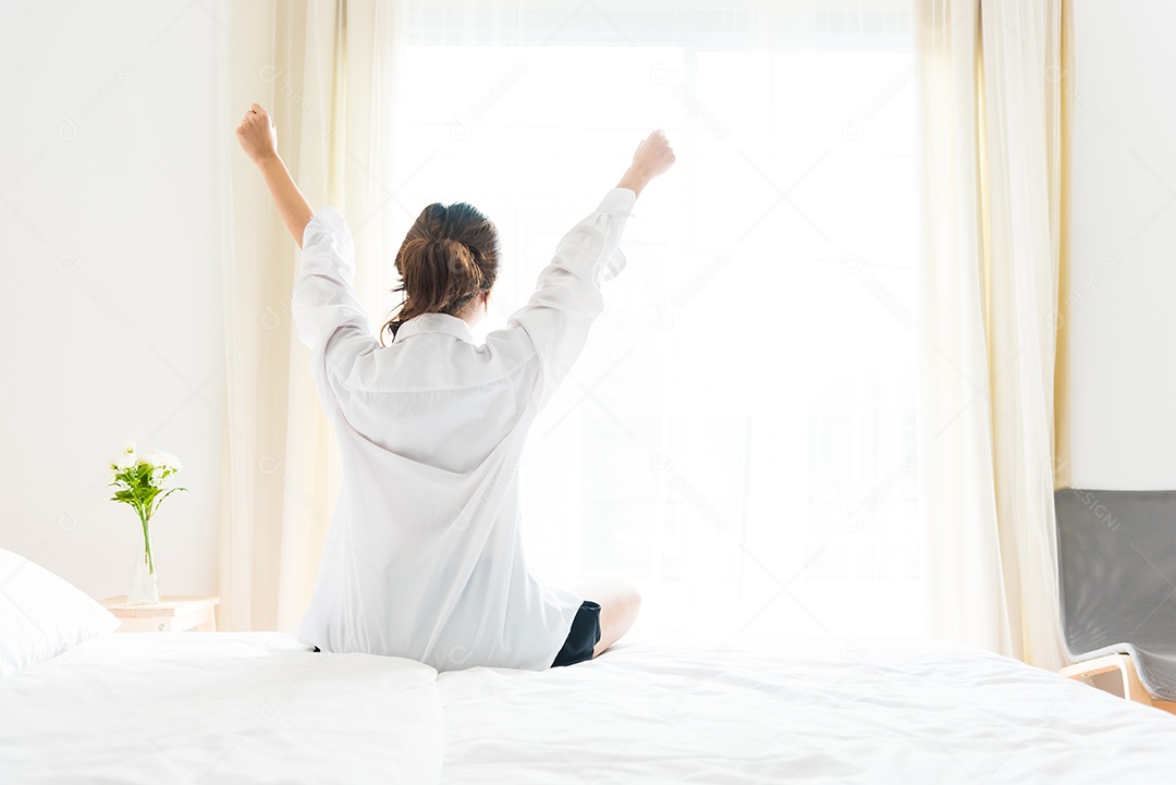 Vista traseira da mulher esticando de manhã depois de acordar na cama perto da janela. Conceito de férias e relaxamento. Dia preguiçoso e conceito de dia de trabalho. Mulher de escritório e trabalhadora no tema da vida diária.