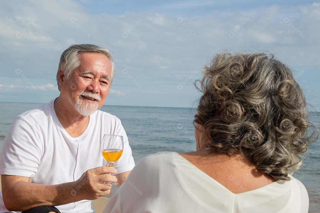 Casal sênior asiático gosta de conversar e beber vinho na praia