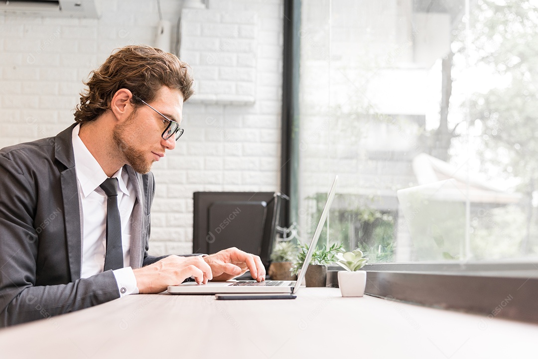 Homem de negócios trabalhando duro com o laptop na mesa no escritório perto da janela. Conceito de negócios e sucesso. Conceito de pessoas e ocupação.