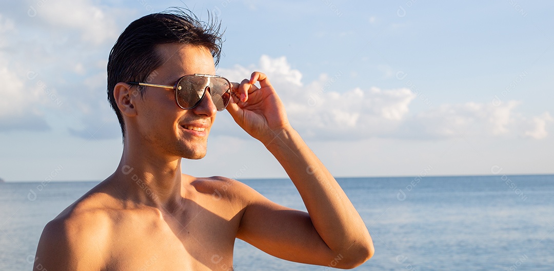 Homem caucasiano em topless usando óculos de sol em pé na praia