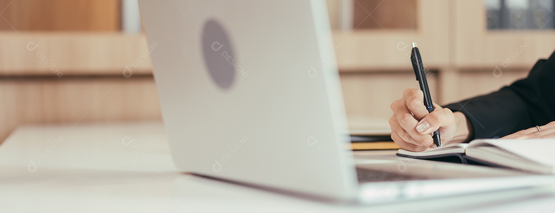 Mão fazendo anotações no caderno enquanto estiver usando o laptop pesquisando