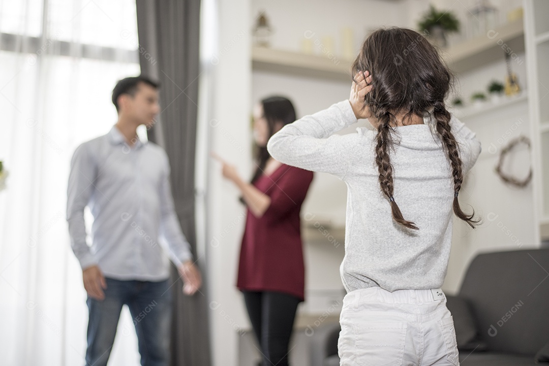 Na visão de trás, a garotinha coloca as mãos nos ouvidos porque não quer ouvir a briga do pai e da mãe. ouvidos fechados, cena dramática familiar, questões de pais, conceito de problema social e de pais.