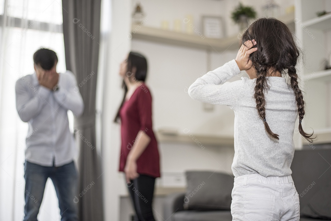Na visão de trás, a garotinha coloca as mãos nos ouvidos porque não quer ouvir a briga do pai e da mãe. ouvidos fechados, cena dramática familiar, questões de pais, conceito de problema social e de pais.