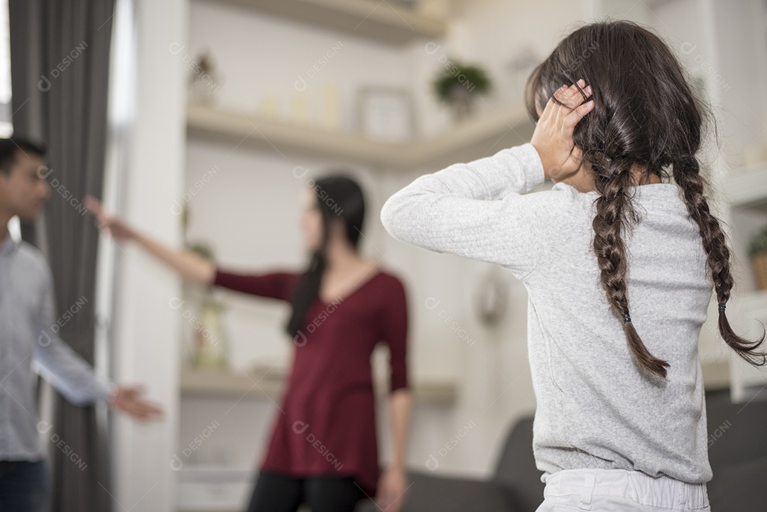 Na visão de trás, a garotinha coloca as mãos nos ouvidos porque não quer ouvir a briga do pai e da mãe. ouvidos fechados, cena dramática familiar, questões de pais, conceito de problema social e de pais.