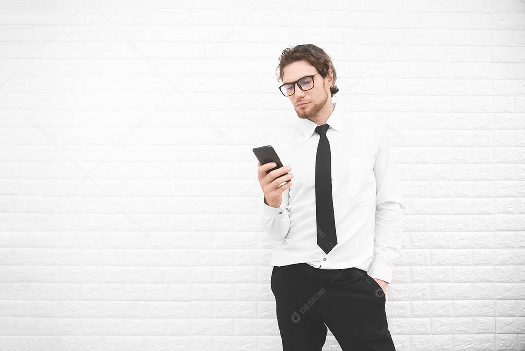 Empresário de uniforme formal e usando smartphone ou celular em frente à parede branca, conceito de negócios e moda.