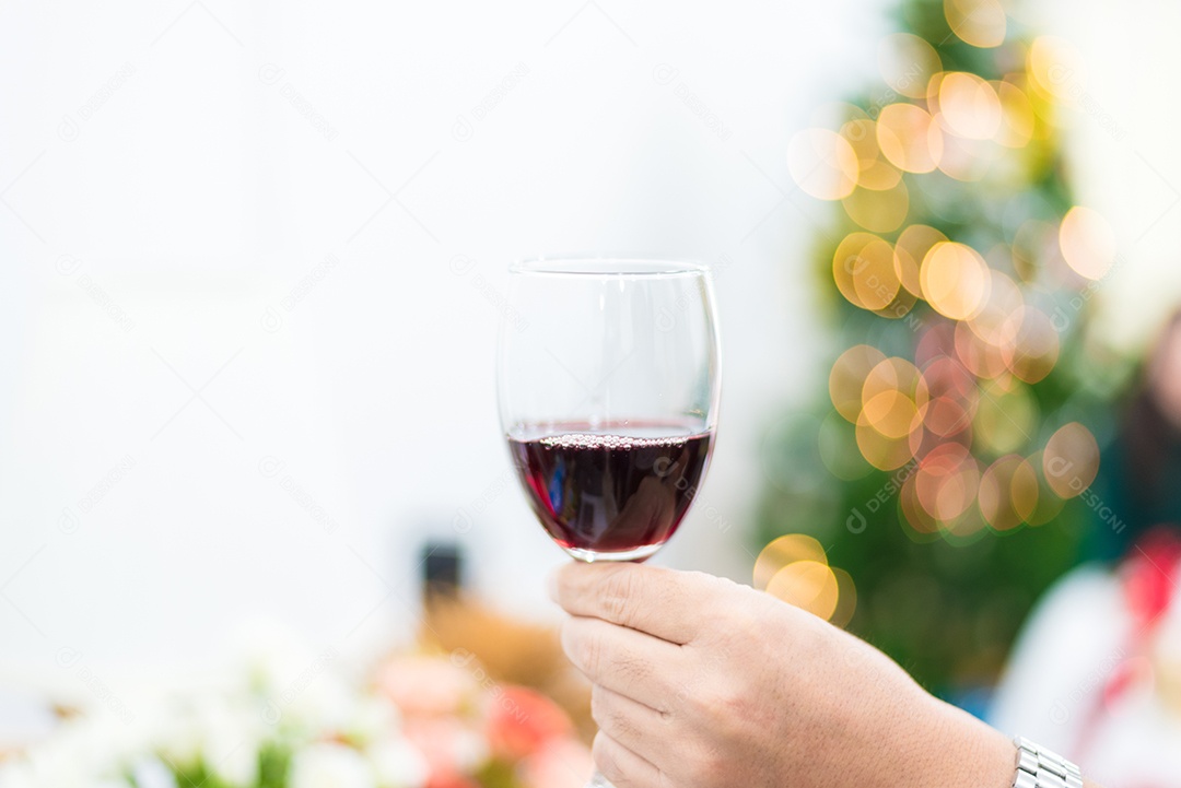 Copo de vinho tinto para brindar em festa com fundo de árvore de Natal.