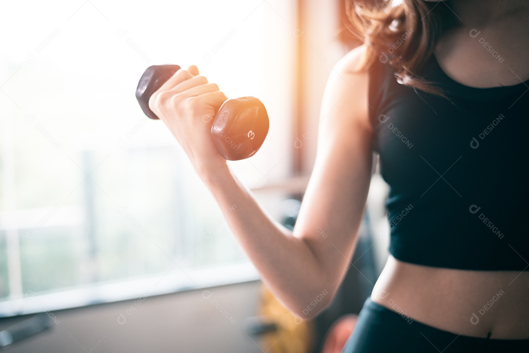 Mão de mulher esportiva levantando halteres para treinamento de peso perto da janela com a mão direita para bombear o músculo bíceps.