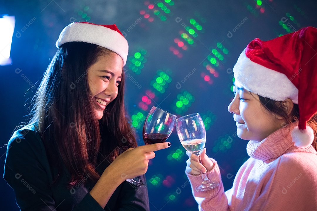 Duas mulheres asiáticas celebrando a festa de Natal e ano novo com taças de vinho no pub.