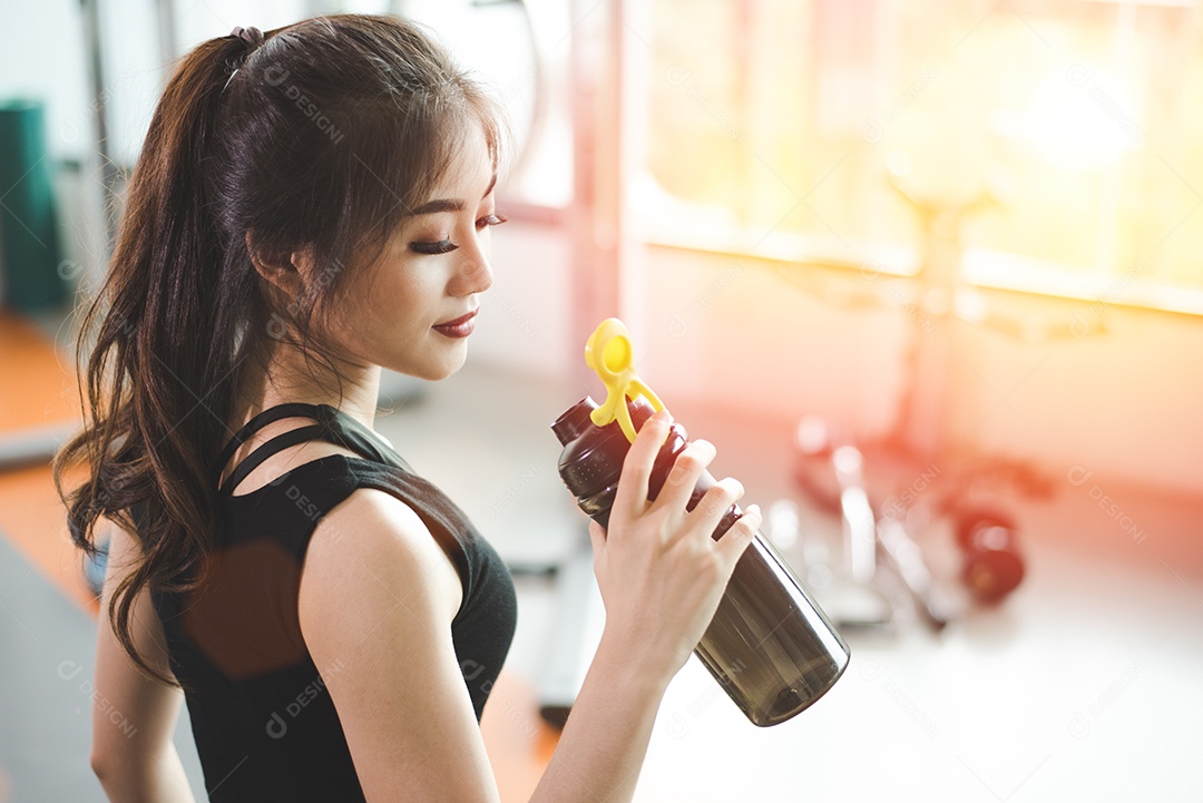 Mulher bonita asiática bebendo shake de proteína ou água potável no ginásio de treinamento esportivo. Conceito de esportes e pessoas.