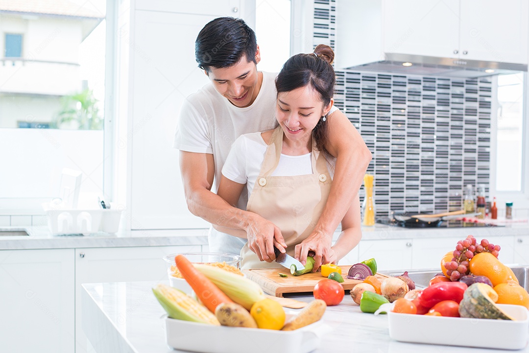 Amantes asiáticos ou casal cozinhando e cortando vegetais na cozinha. Homem e mulher se olhando em casa. Conceito de férias e lua de mel.