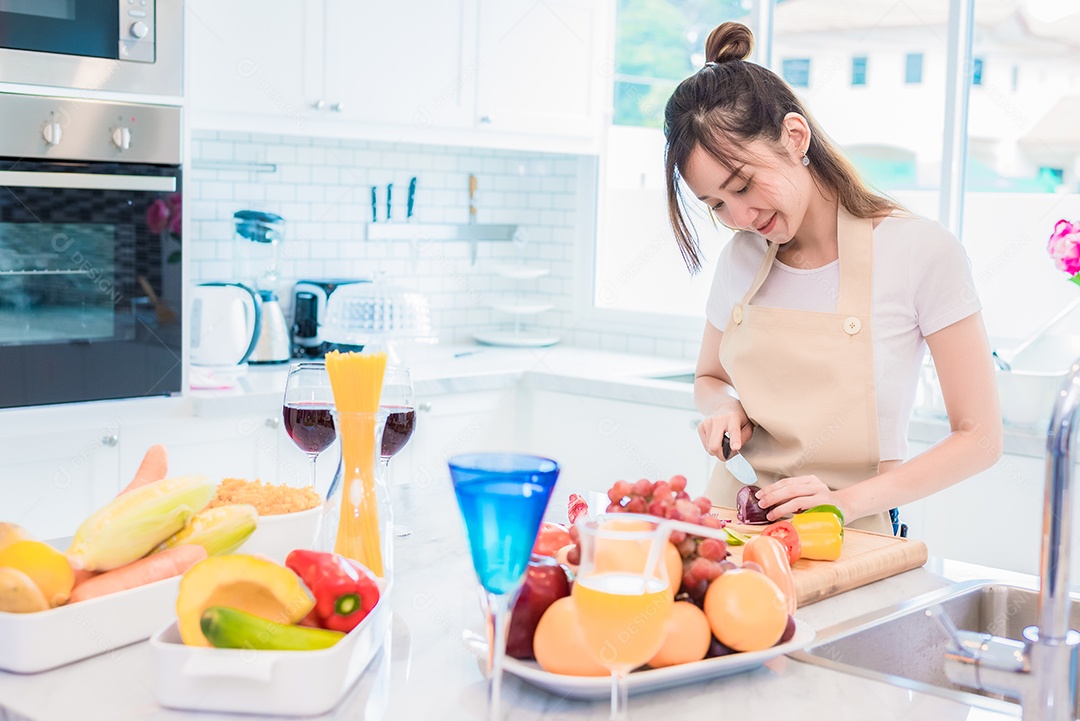 Mulher cozinhando e cortando vegetais na sala da cozinha cheia de comida e frutas na mesa. Conceito de férias e felicidade.